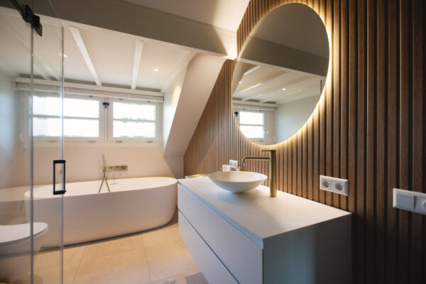 Badkamer met ligbad en houten wandbekleding en ronde spiegel – villa Het Gooi